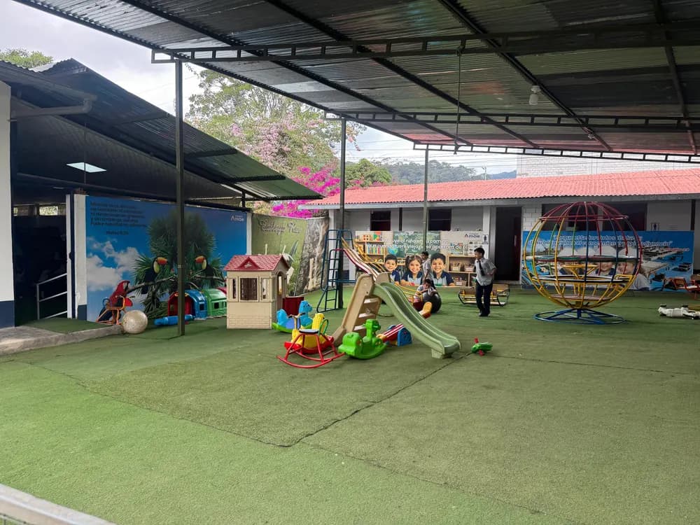 Niños de inicial jugando en el patio techado, con juegos, casita y grass sintético.